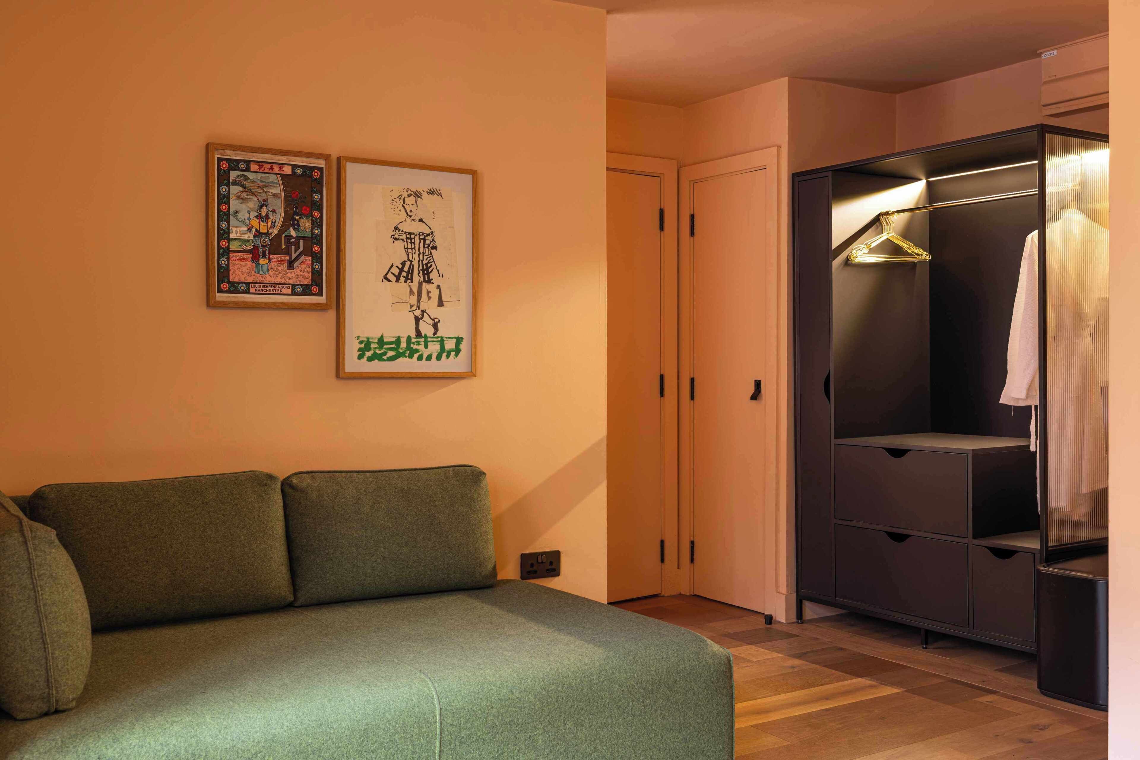Una habitación con un sofá verde, un armario con perchero y dos cuadros en la pared.