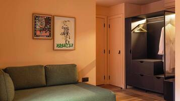 A room with a green sofa, a wardrobe with a hanging clothes rack, and two framed pictures on the wall.