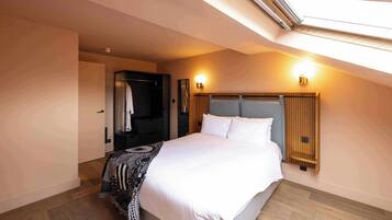 Een slaapkamer met dakraam, een bed met witte beddengoed, een houten hoofdeinde en een nachtkastje.
