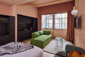 A modern hotel room with a green sofa, a bed, a small table with a vase, and a large window with curtains. - Whitworth Locke (Manchester)
