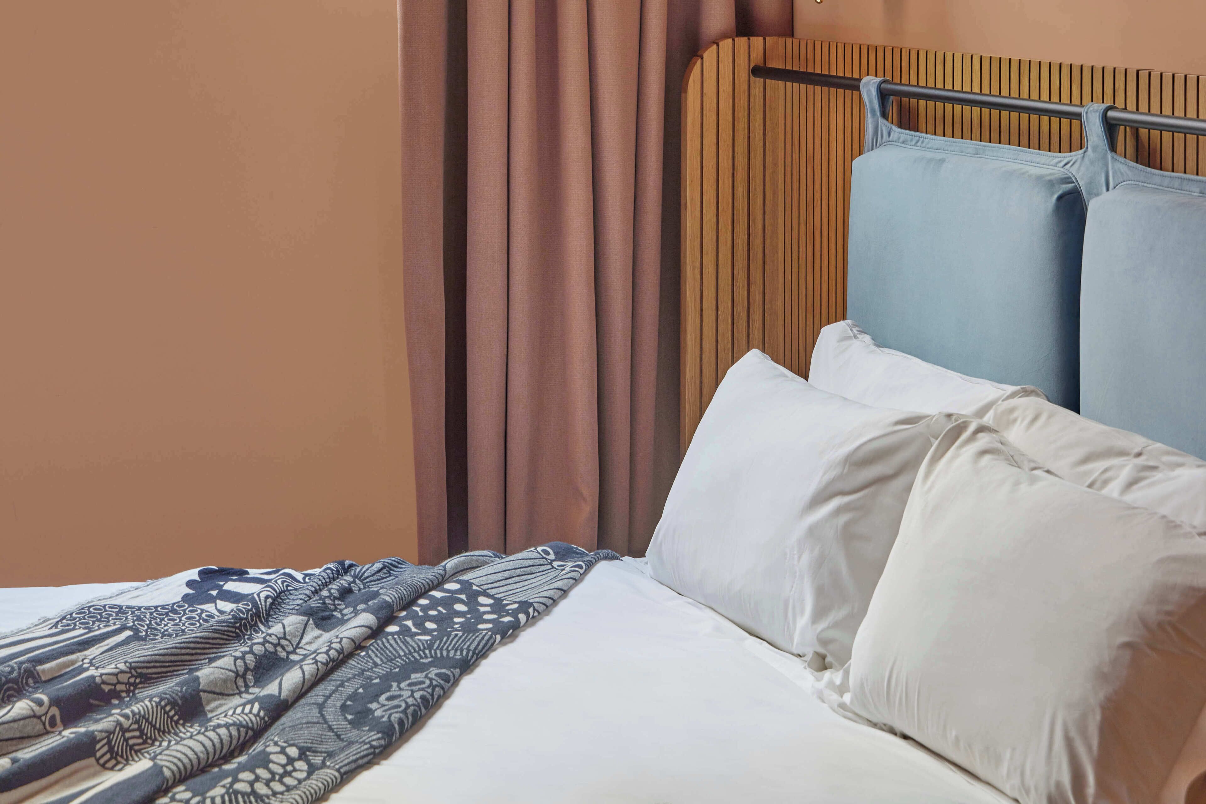 Una cama bien tendida con ropa de cama estampada, un cabecero con una barra horizontal y una ventana con cortinas.