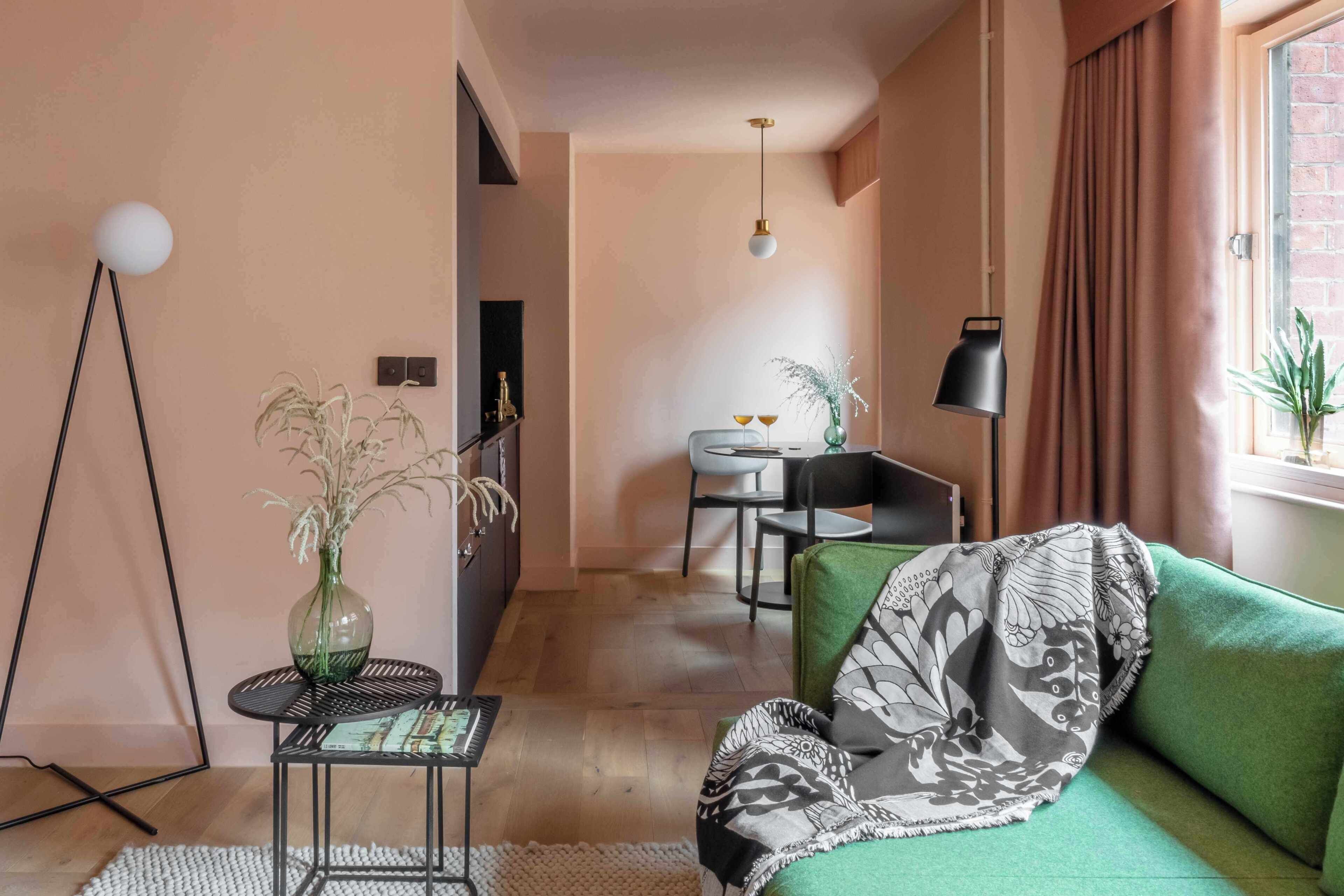 A modern living room with a green sofa, a small round table with a vase, and a floor lamp.