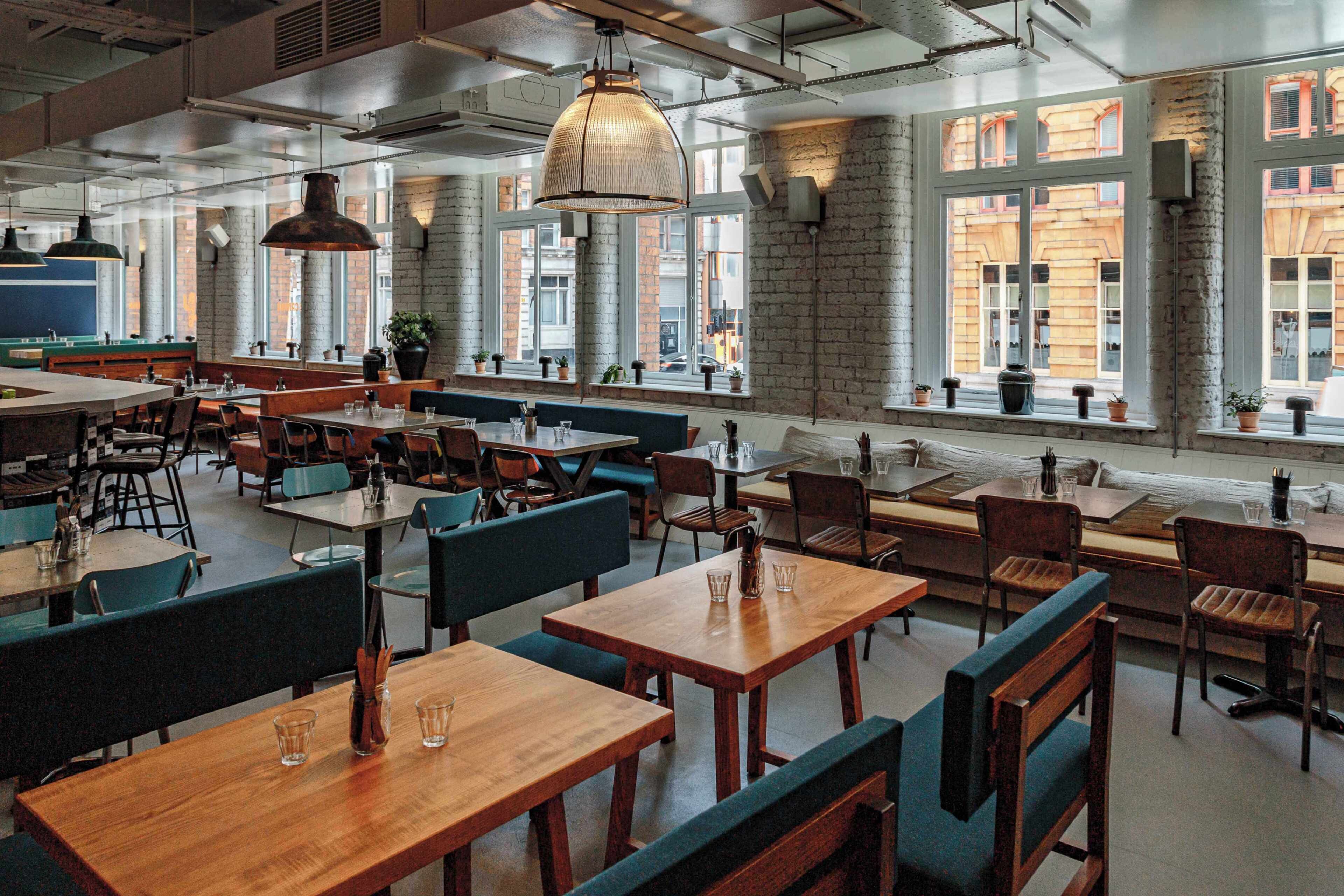 A spacious restaurant with high ceilings, exposed brick walls, and large windows offering views of the street.