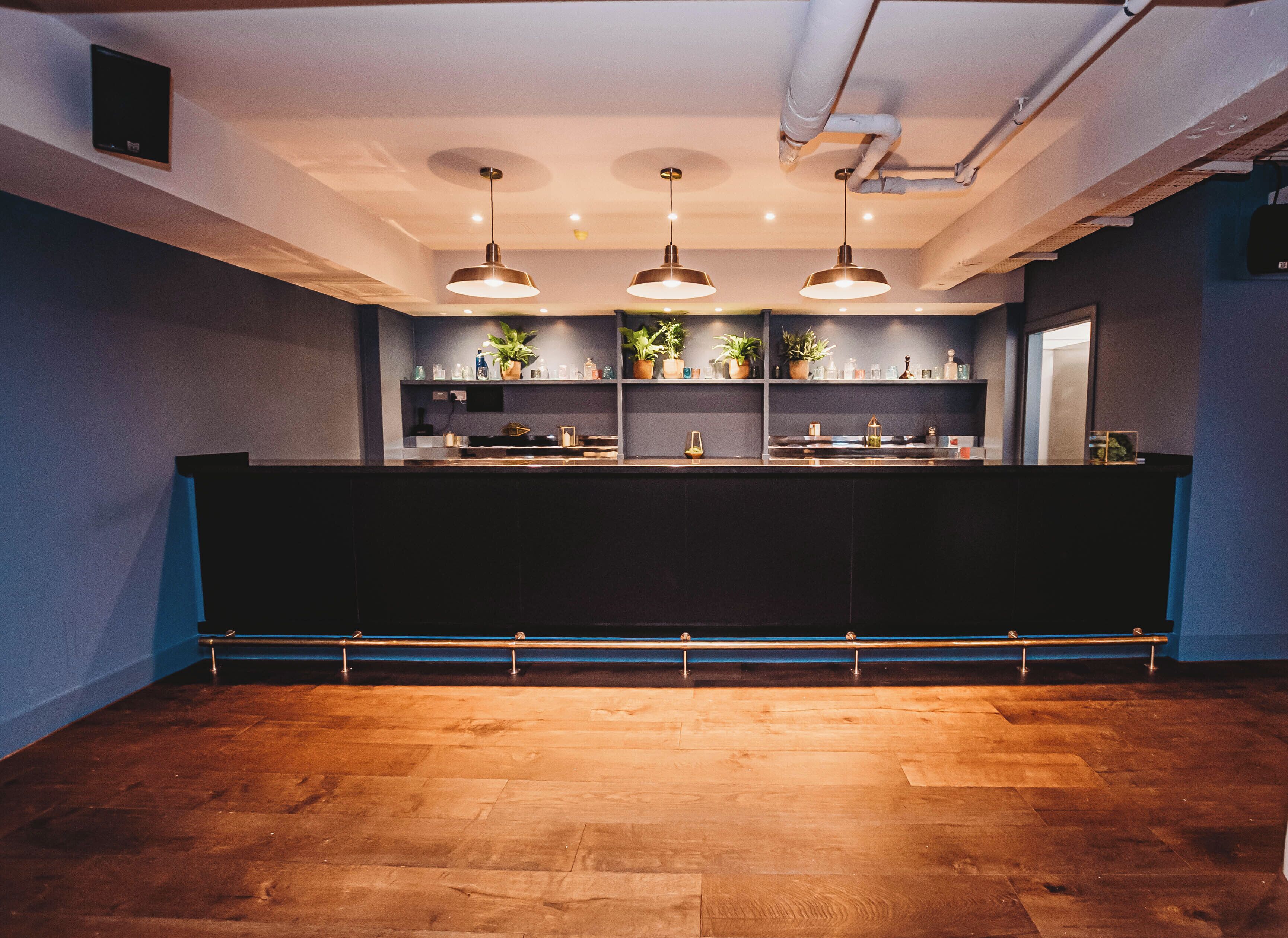 A reception area with a dark counter, three pendant lights, potted plants, and a wooden floor.