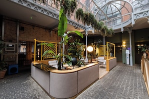 Un hall d’hôtel comprenant un comptoir d’accueil, un espace salon et des plantes suspendues.