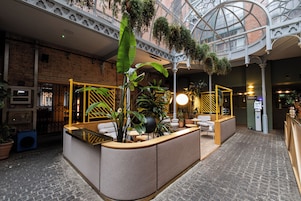 Vestíbulo de hotel con recepción, zona de estar y plantas colgantes.