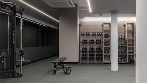 A gym with weightlifting equipment, a bench, and a wall-mounted rack of dumbbells.