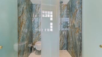 Un baño con puerta de vidrio, paredes de mármol, inodoro y zona de ducha.