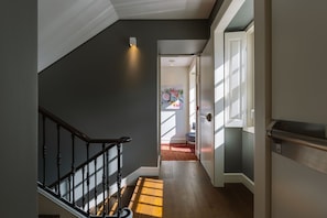Una escalera con una pared oscura y un suelo de tonos claros, que conduce a una habitación con una puerta y un ventanal.