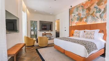 Een moderne hotelkamer met een groot bed, een flatscreen televisie, een zithoek met twee stoelen en een groot abstract schilderij aan de muur.