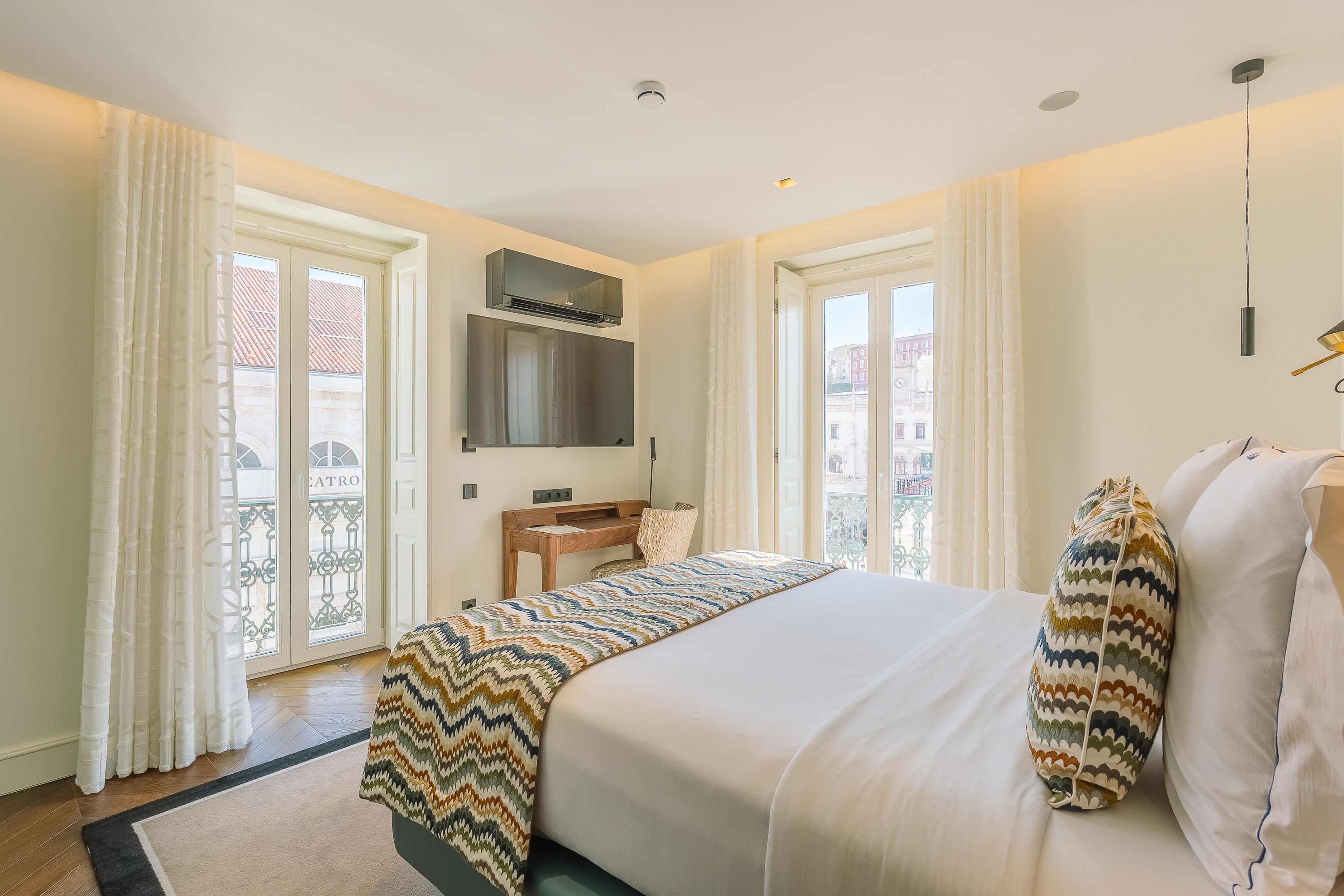 Een hotelkamer met een bed, een bureau, een stoel, een televisie en een balkon met gordijnen.