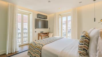 Een hotelkamer met een bed, een bureau, een stoel, een televisie en een balkon met gordijnen.