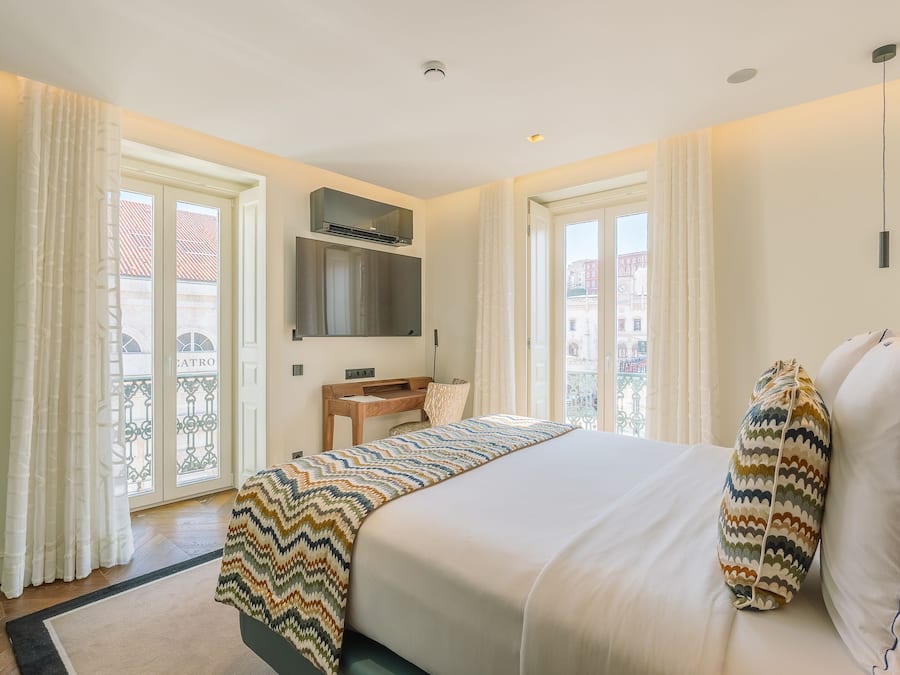 Une chambre d’hôtel avec un lit, un bureau, une chaise, une télévision et un balcon avec des rideaux.
