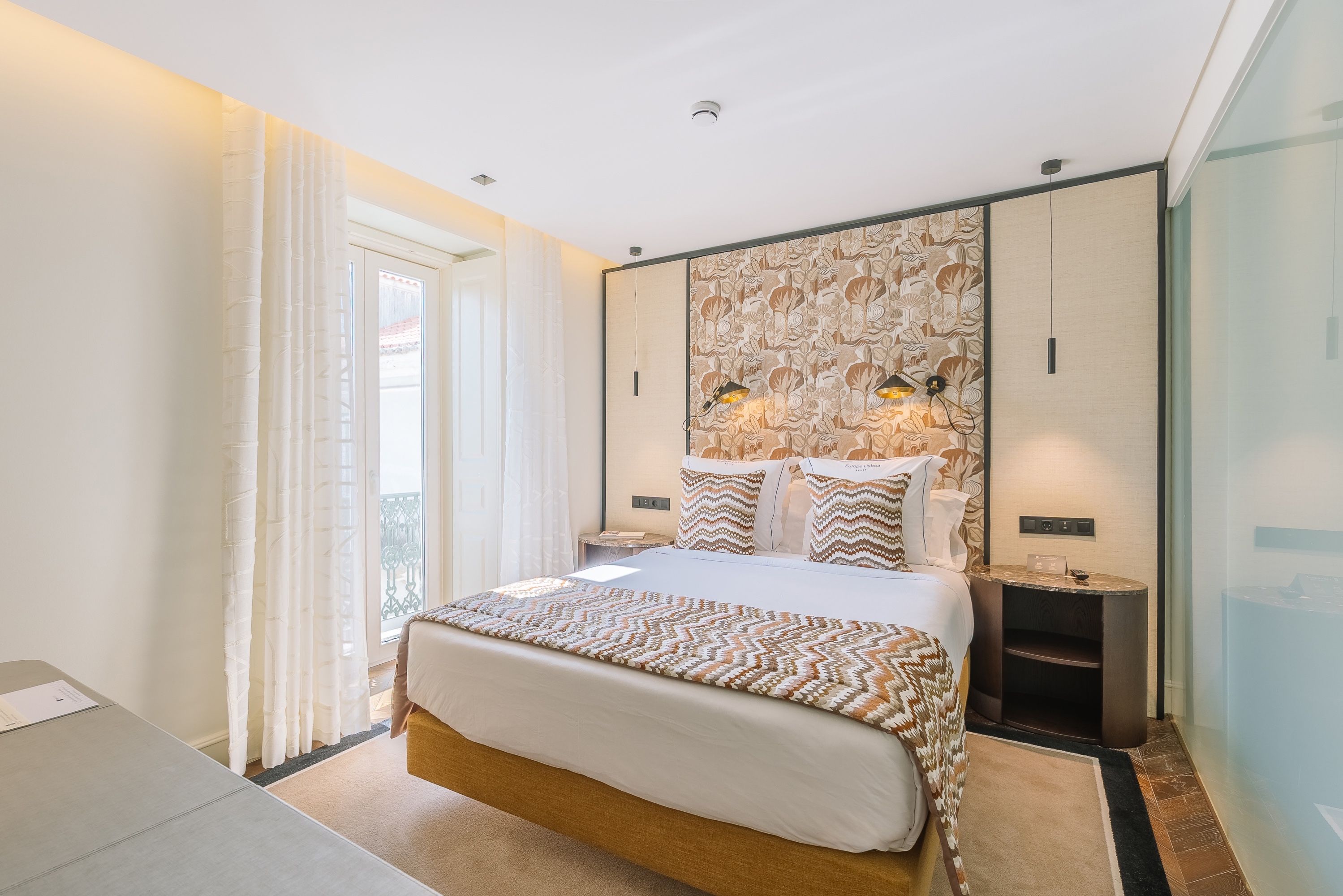 Una habitación de hotel moderna con una cama grande, un armario, una mesita de noche y vistas al exterior.