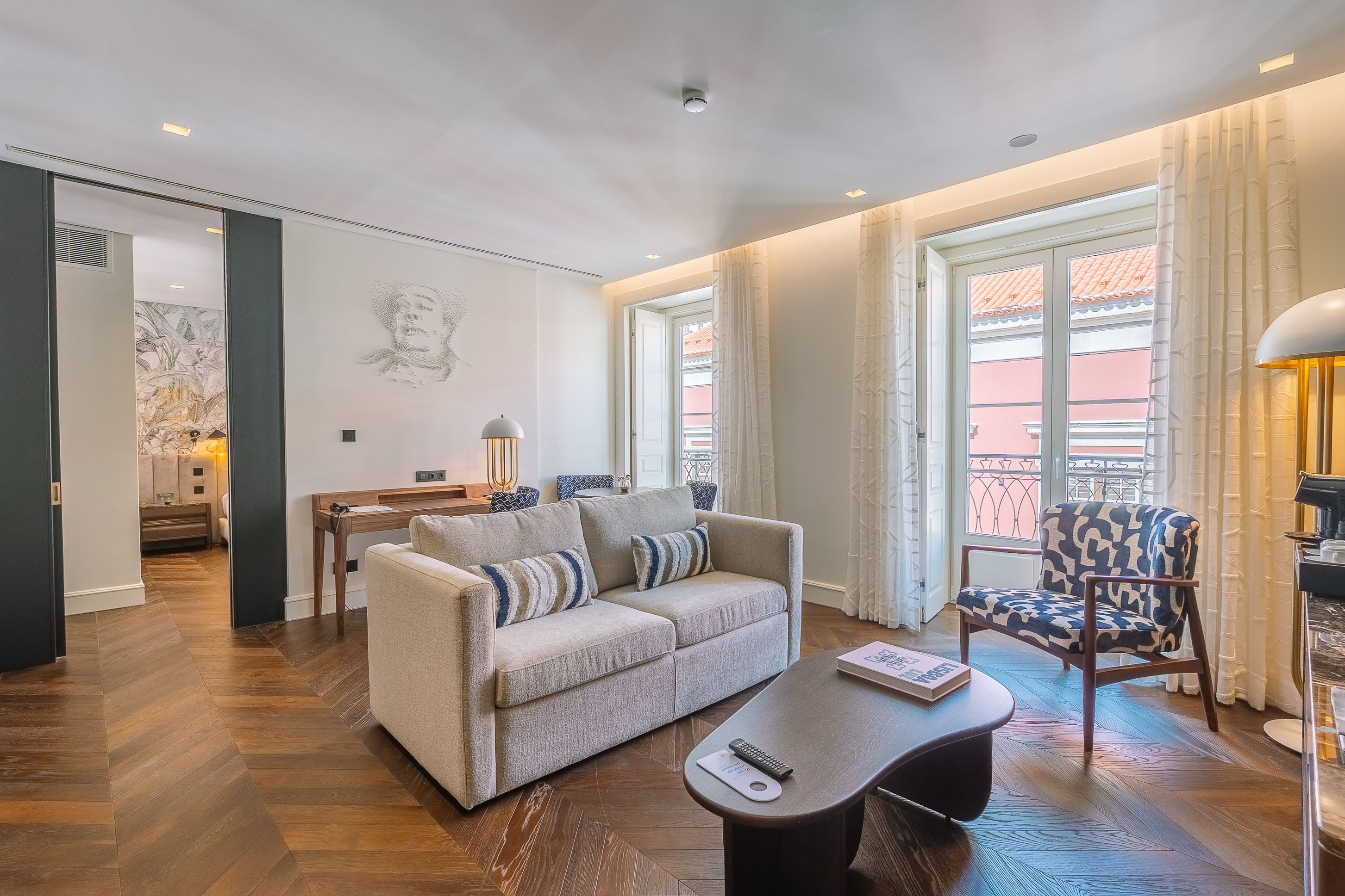 Een moderne woonkamer met een bank, fauteuil en salontafel, een eethoek met tafel en stoelen, en grote ramen met gordijnen.