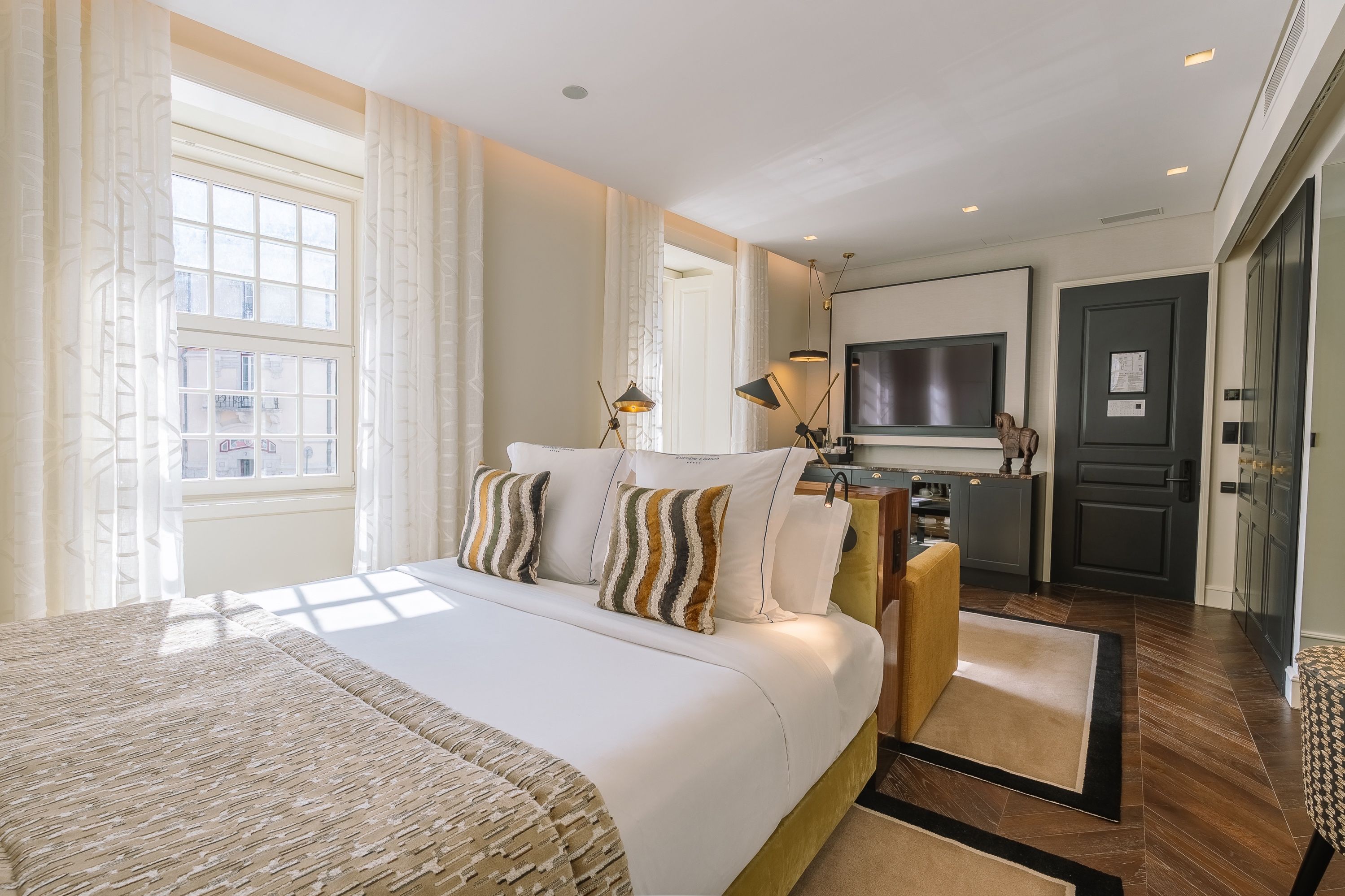A hotel room with a large bed, a TV, a desk, and a view of the city.