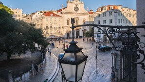 Uma praça de pedra com edifícios históricos, uma igreja destacada e um poste de rua tradicional.