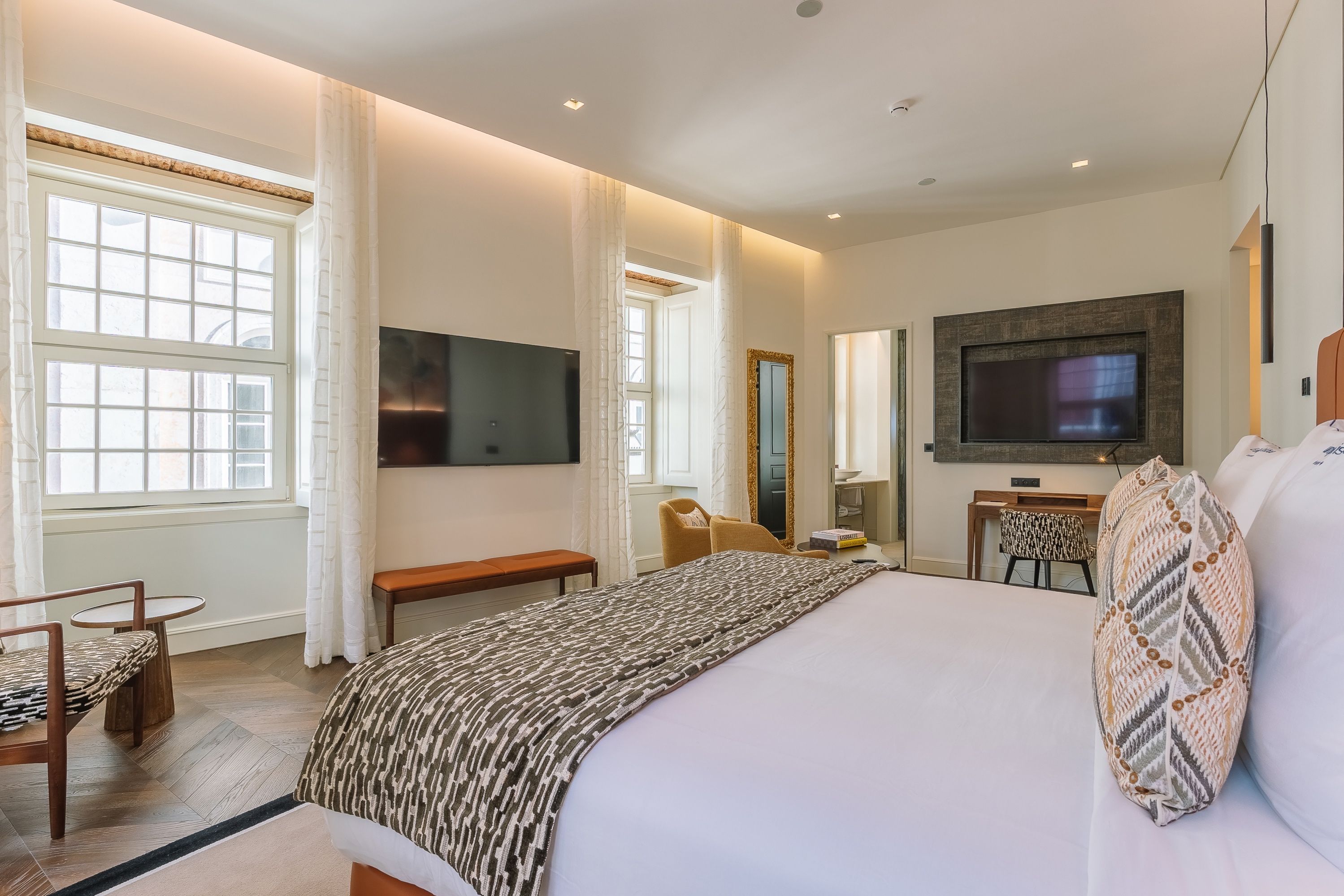 A hotel room with a large bed, a desk, a chair, a television, and a window.