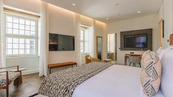 A hotel room with a large bed, a desk, a chair, a television, and a window.