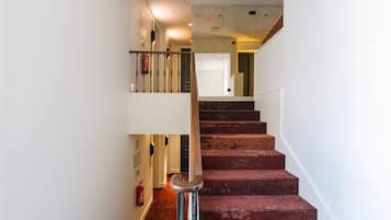 Una escalera con peldaños alfombrados de rojo, barandilla de metal y extintor en la pared.
