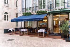 An outdoor seating area with tables and chairs, a blue awning, and a building with decorative tiles. - Europe Lisboa Boutique Hotel (Lisbon)
