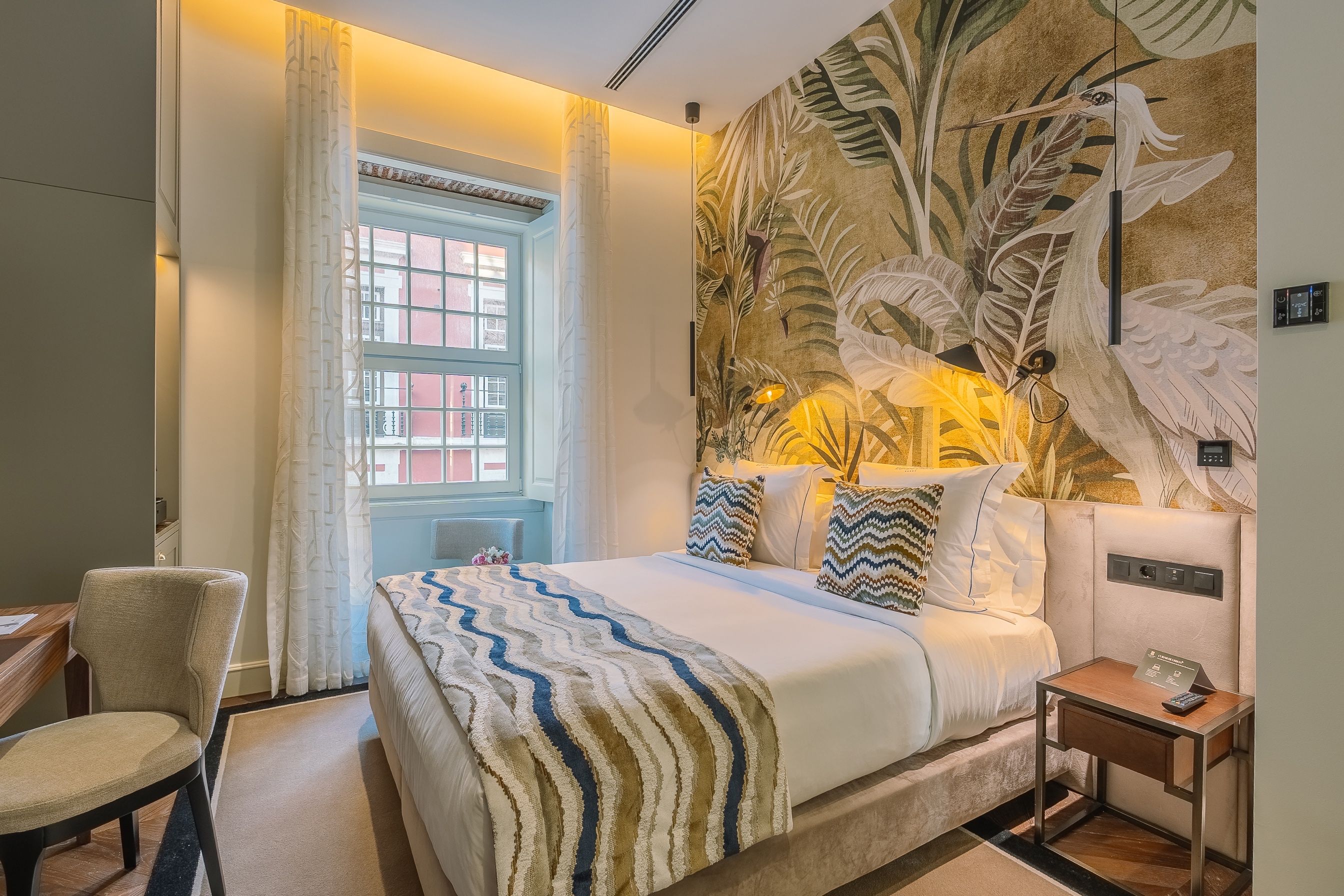 A hotel room with a bed, a chair, a desk, and a large window.