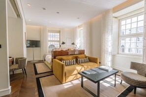 Una habitación de hotel moderna con sofá, mesa de centro, televisor y escritorio con silla.
