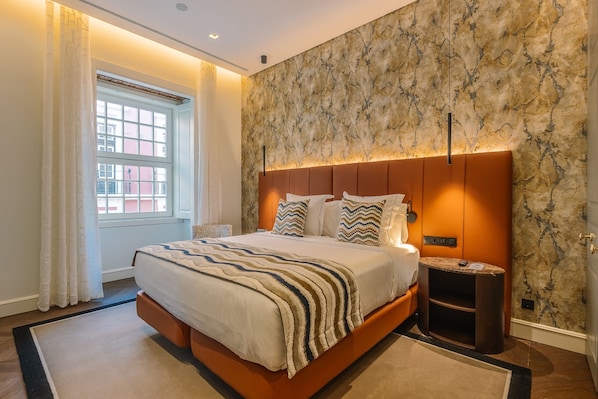 Ein modernes Hotelzimmer mit einem großen Bett, einem Nachttisch, einem Fenster mit Vorhängen und einer Wand mit Marmoroptik.