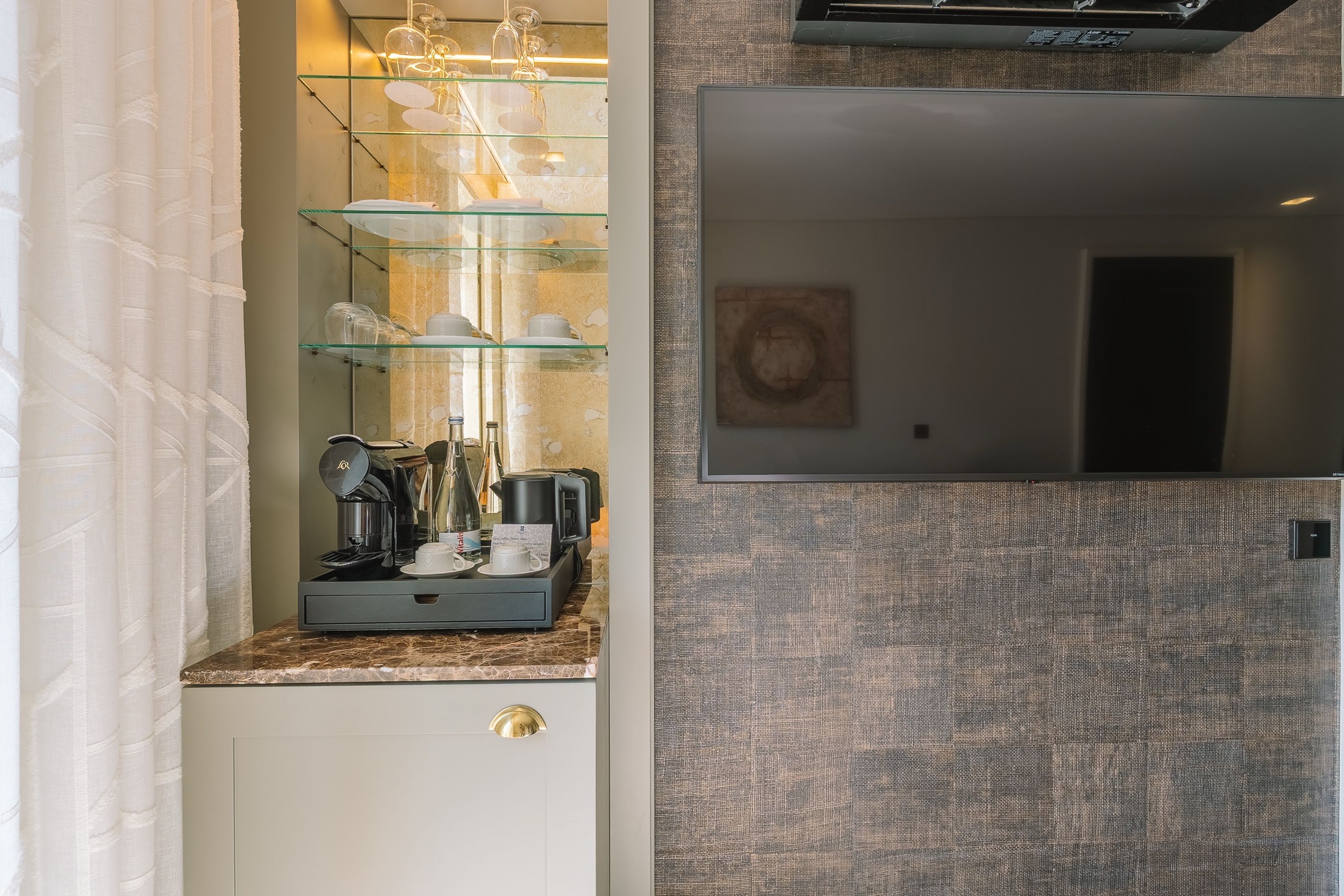 Cocina compacta con cafetera, repisa de vidrio con tazas y espejo encima.
