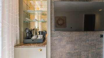 Cocina compacta con cafetera, repisa de vidrio con tazas y espejo encima.