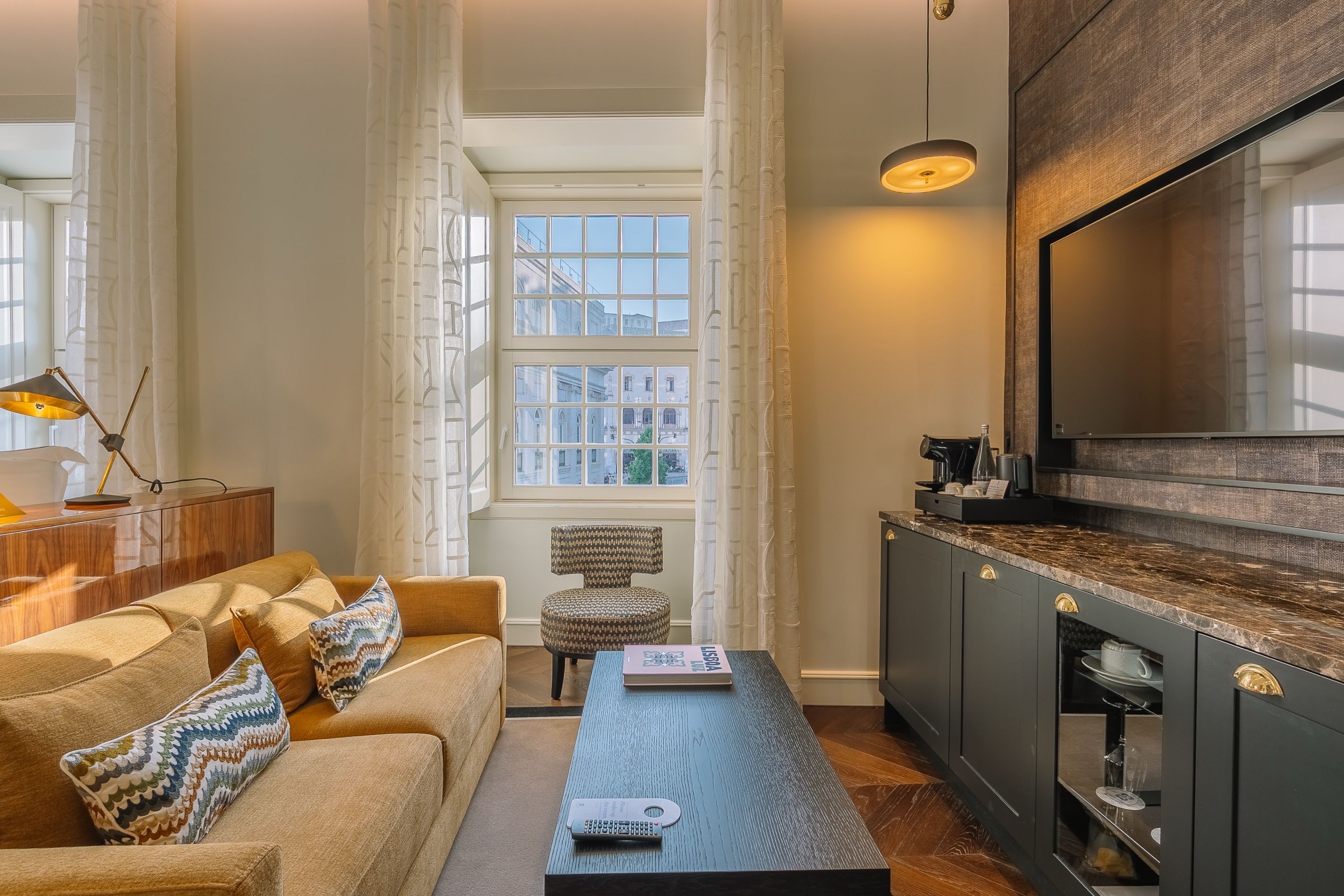 A modern living room with a sofa, a coffee table, a television, and a kitchen area with a large screen.