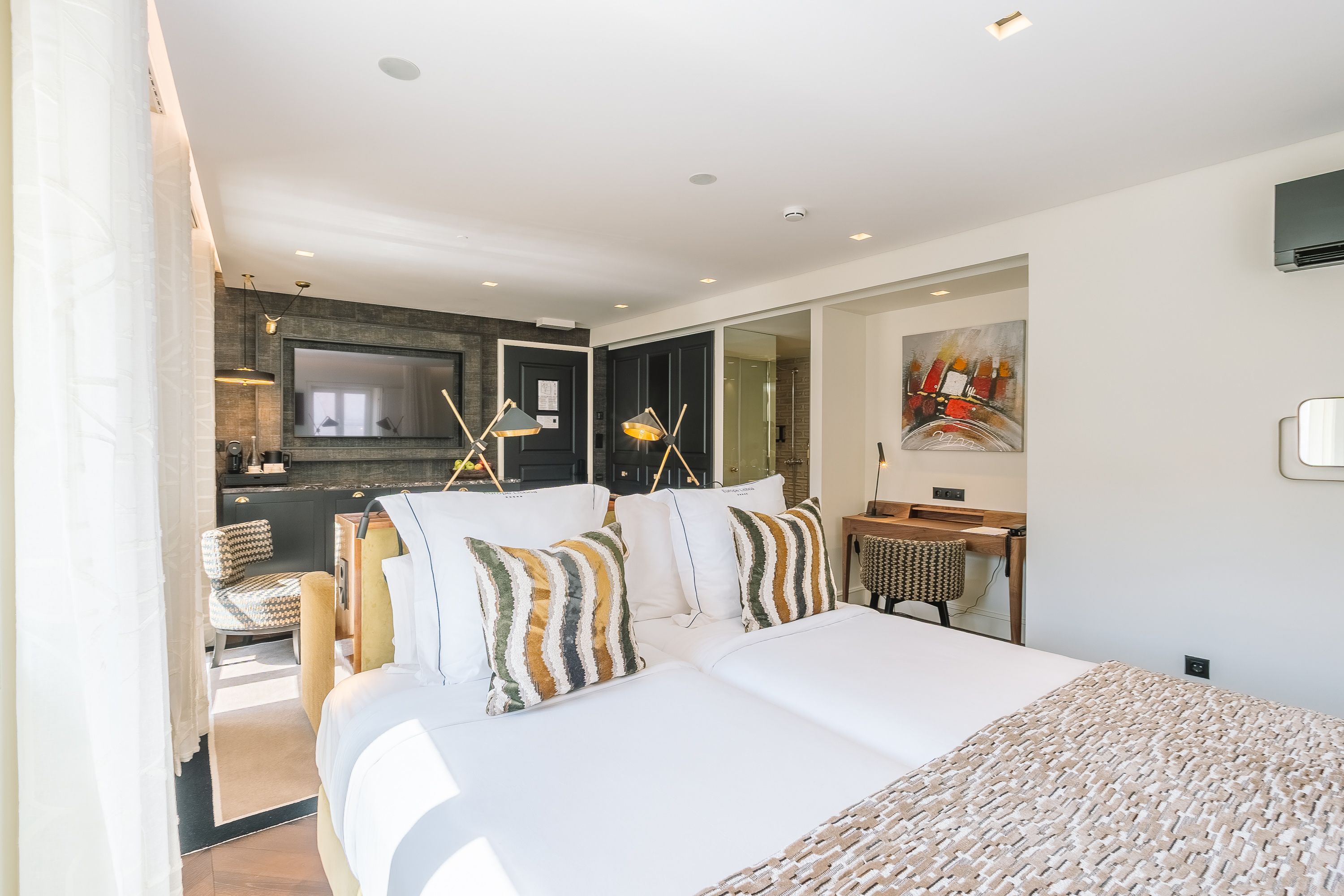 A modern hotel room with a large bed, a desk, and a bathroom visible through a glass door.