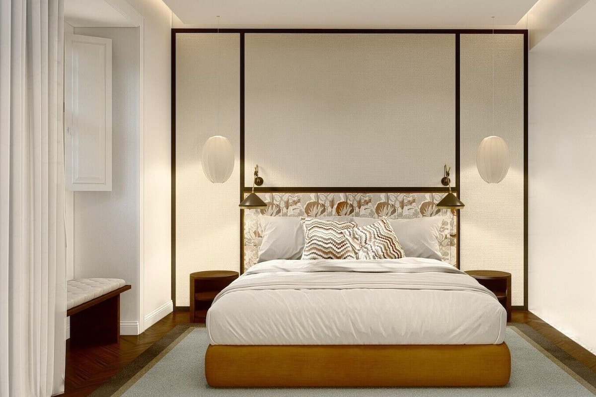 Un dormitorio con una cama grande, dos mesitas de noche, un banco e iluminación de pared.