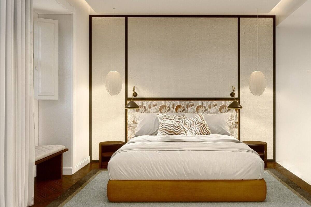 A bedroom with a large bed, two bedside tables, a bench, and a wall-mounted light fixture.