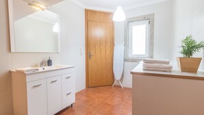 A modern bathroom with a wooden door, a large mirror, a sink with a soap dispenser, a towel rack, and a potted plant.