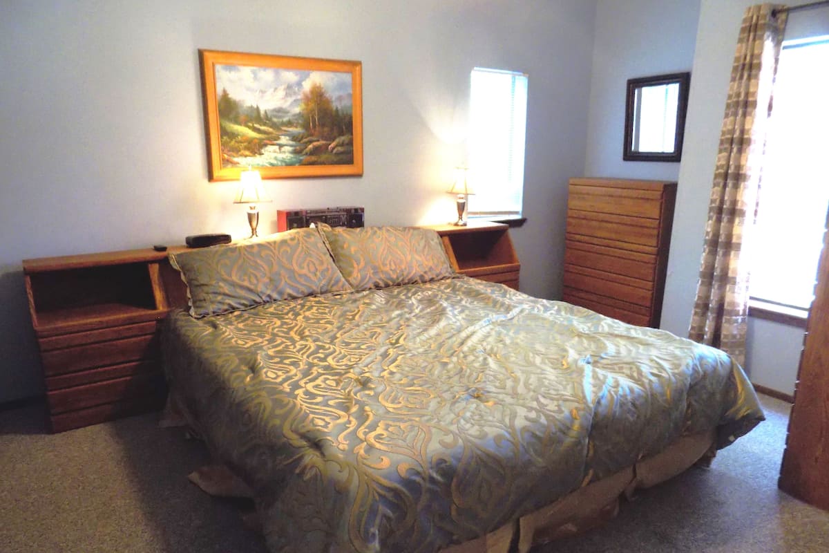 A bedroom with a bed, wooden dresser, nightstands, and a painting on the wall.