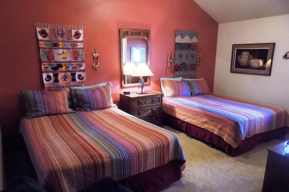 A bedroom with two beds, a nightstand, a mirror, and wall decorations.