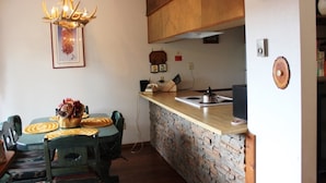 A dining area with a wooden table and chairs, a chandelier, and a kitchen counter with a sink and stove. - Angel Fire Chalet (Angel Fire)