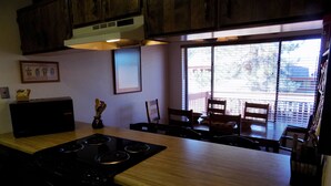A kitchen with wooden cabinets, a built-in stove, and a dining area with chairs and a table. - Angel Fire Chalet (Angel Fire)