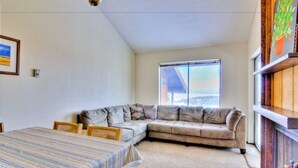A room with a large window, a sofa, a dining table, and a bookshelf. - Bella Vista (Angel Fire)