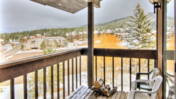 A balcony with a wooden railing, a view of a snowy landscape, and a pile of firewood. - Bella Vista (Angel Fire)
