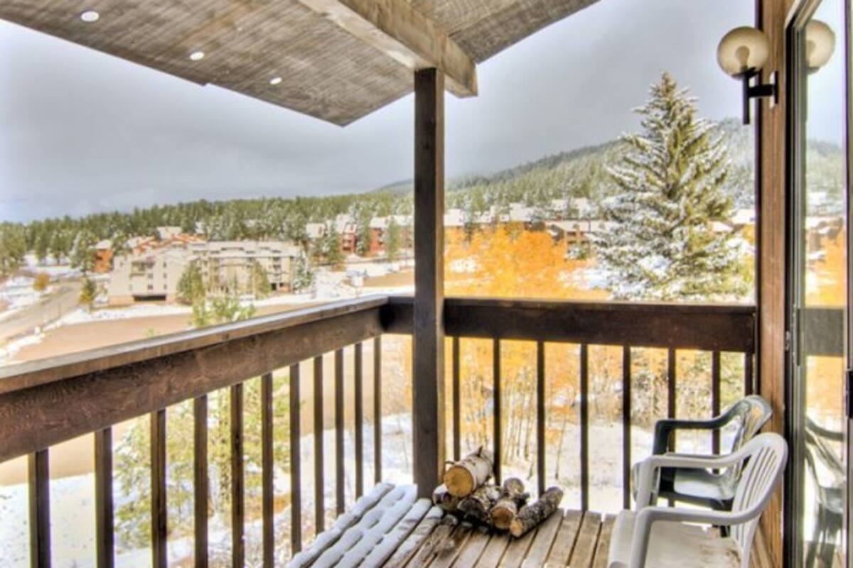A balcony with a wooden railing, a view of a snowy landscape, and a pile of firewood.