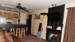 A living room with a leather couch, a fireplace, and a kitchen area in the background. - Bella Vista (Angel Fire)