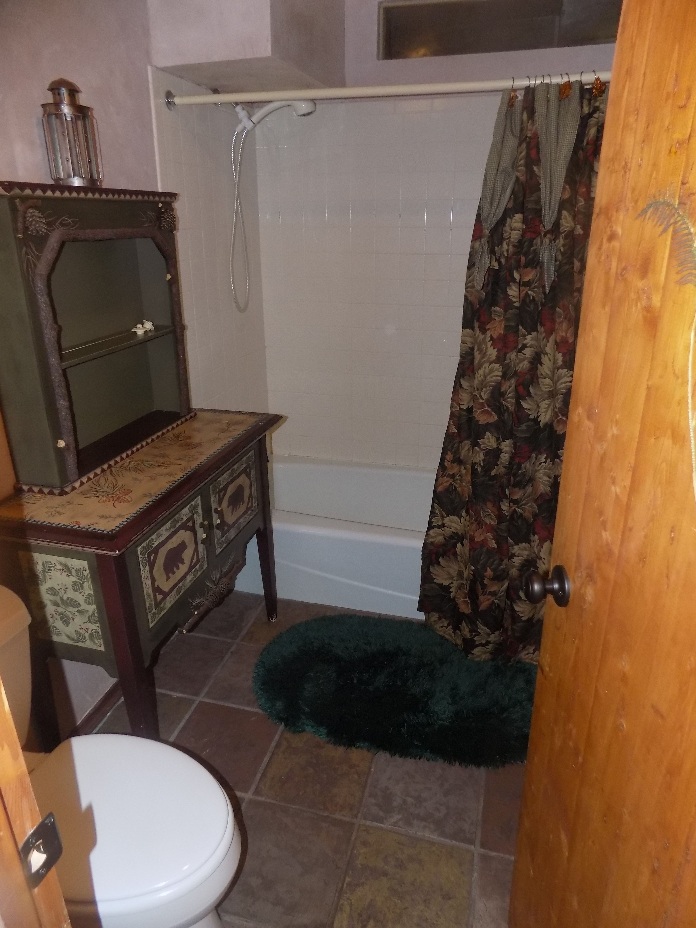 A bathroom with a toilet, a wooden vanity with a mirror, a bathtub, and a shower curtain.