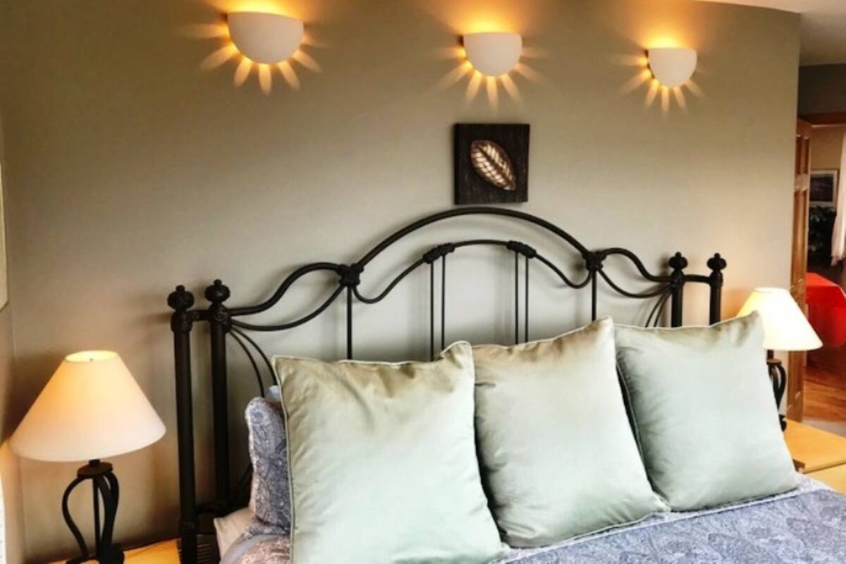 A bedroom with a bed, two wall-mounted lamps, and a framed artwork on the wall.