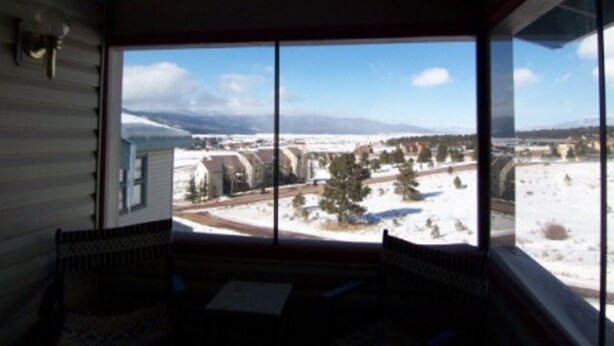 A room with a large window offering a view of a snowy landscape and buildings. - Benchmark (Angel Fire)