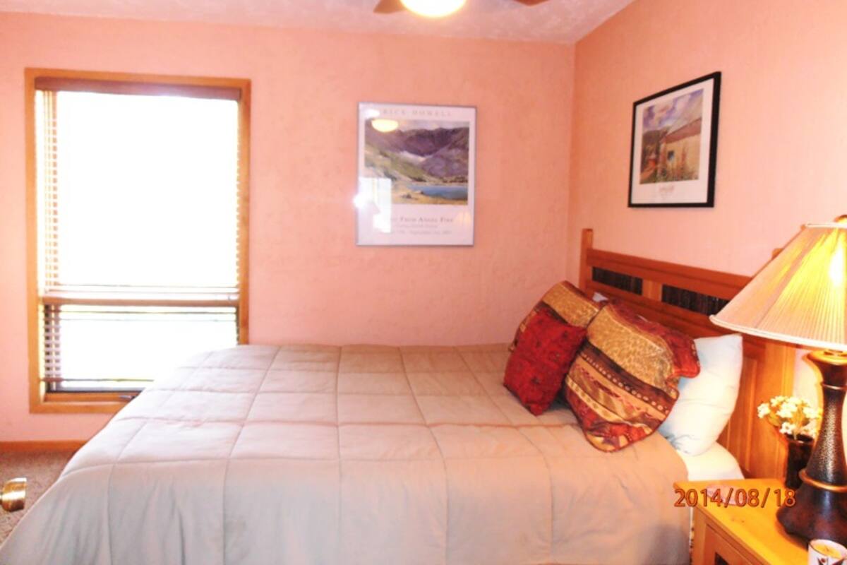 A bedroom with a bed, a ceiling fan, a window, and a nightstand with a lamp.