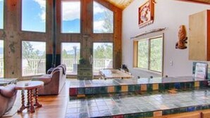 A spacious room with large windows, a wooden ceiling, and a tiled floor. - Country Club Homes (Angel Fire)