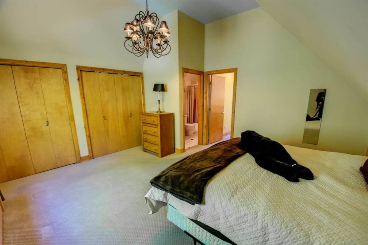 A bedroom with a large bed, wooden wardrobes, a dresser, a mirror, and a chandelier.
