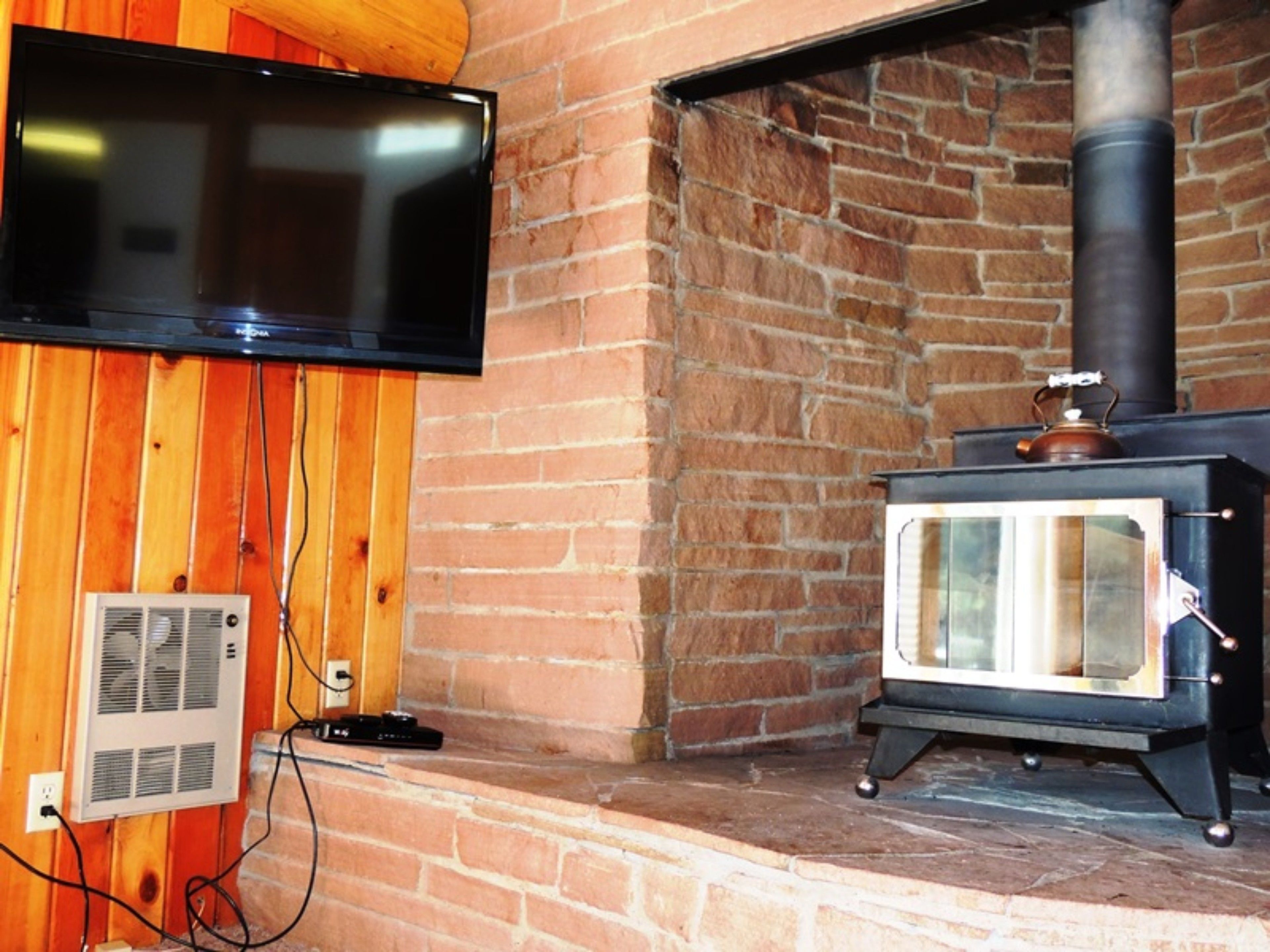 A room with a brick wall, a television mounted on the wall, and a wood-burning stove.